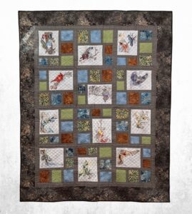 Handmade embroidered woodland quilt with forest bird and nature panels, earthy patchwork blocks in blue, green, rust, cream, and brown, and a dark bark-textured border.
