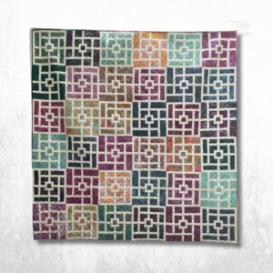 Handmade queen size geometric patchwork quilt with jewel tone batik blocks, white maze-like sashing, and modern square block design hanging outdoors in a wooded setting.