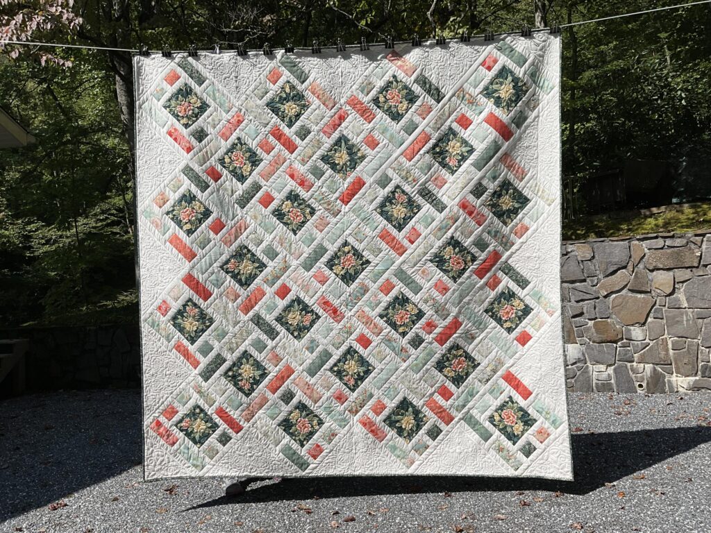 Quilt in diamond pattern with floral centerpieces framed by subtle green and coral hues, all set against a crisp antique white background.