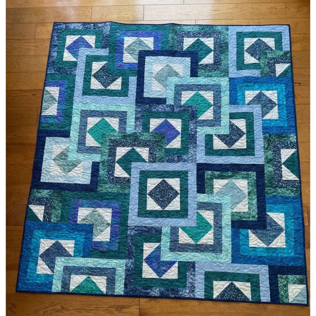 Handmade quilt with modern design of stacked blocks in shades of blue and green.