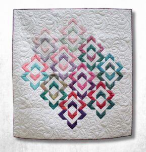 Square handmade baby quilt with colorful linked diamond blocks fading from jewel tones to pastels on a cream quilted background, shown full flat.
