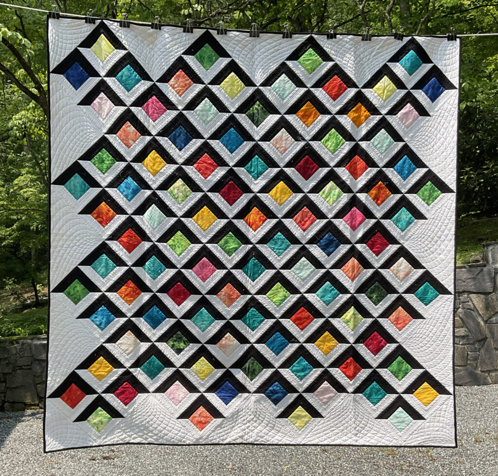 This handmade queen-sized quilt features a striking modern layout of bright, gemstone-colored blocks framed in crisp black and white.