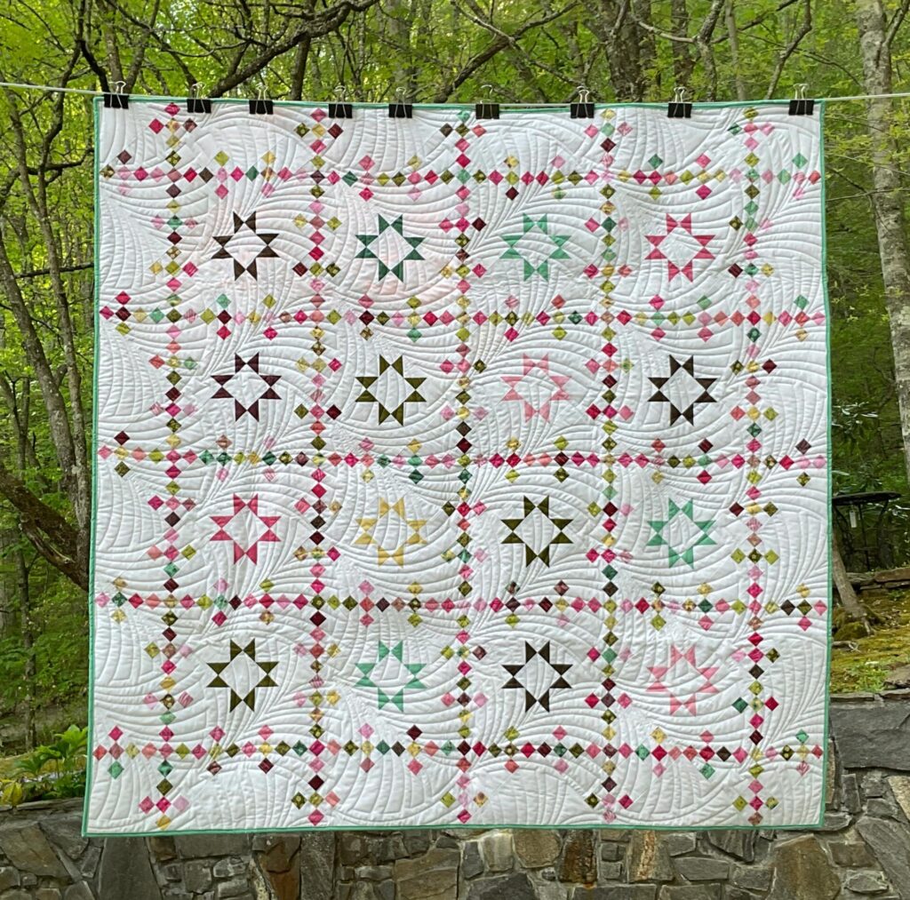 Quilt with traditional styling of pieced stars and chains in bright colors on a white background.