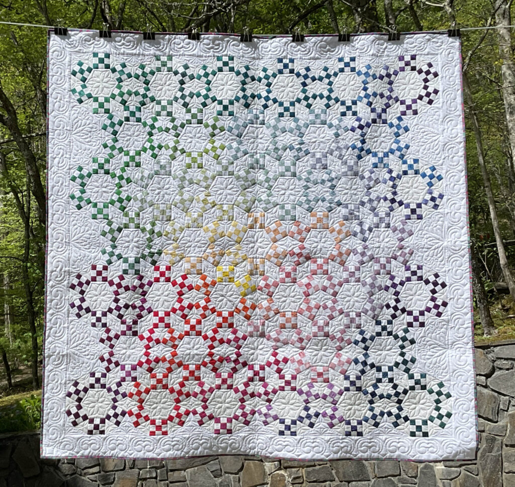 Quilt in linked rings pattern with a modern twist of rainbow hues against a bright white background.