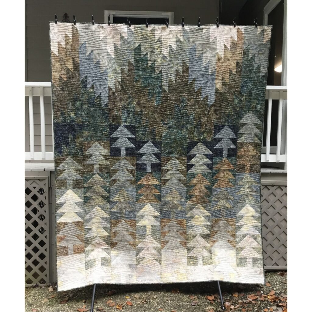 Handmade quilt with stylized trees and mountains in shades of cream, grey and brown,