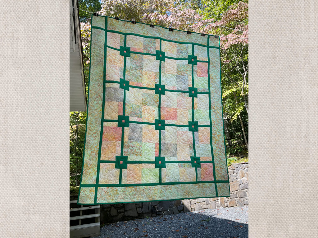 Serene quilt features soft hues of peach, green, and yellow, framed by bold green sashing.