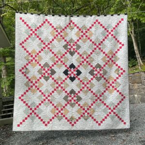King size handmade heart quilt hanging outdoors with neutral hearts on a pale grey background, red patchwork chains, and allover swirl quilting.